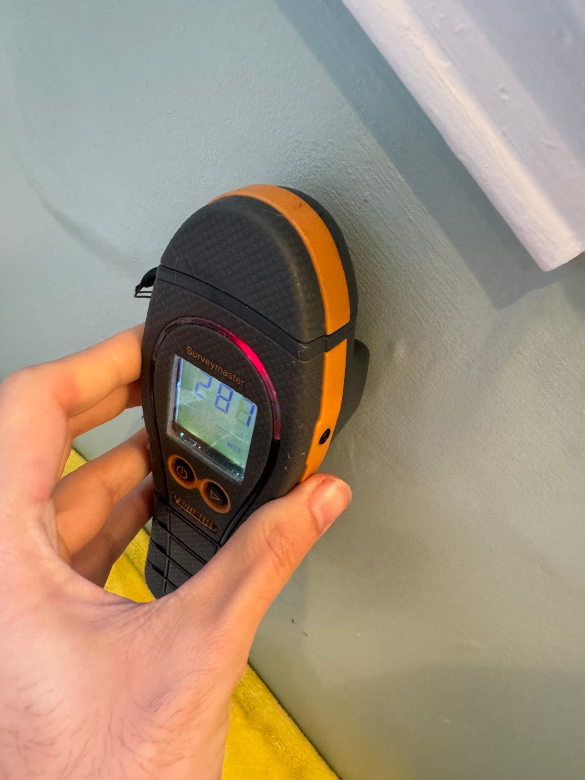 Inspector holding a moisture meter against a wall to check for elevated moisture