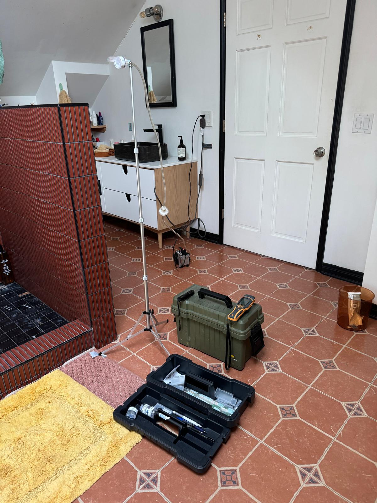 Air sampling pump on a tripod and sampling case set up in a bathroom during an inspection